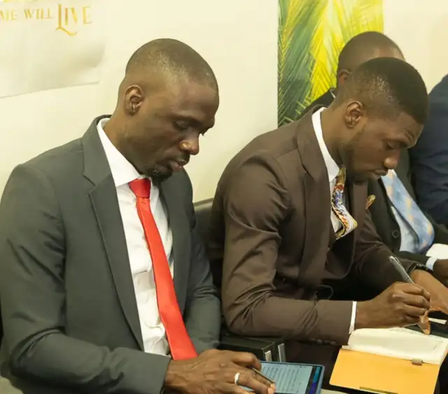 Two men in suits writing in their notebooks during a teaching session