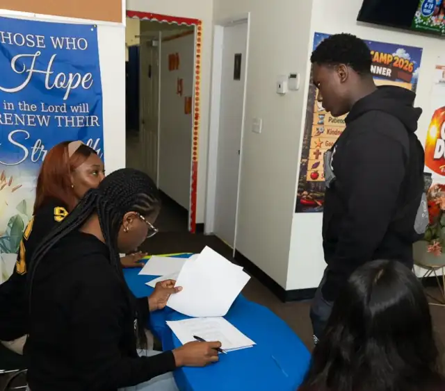 Two volunteers at the welcome desk signing in a young man as he arrives for camp